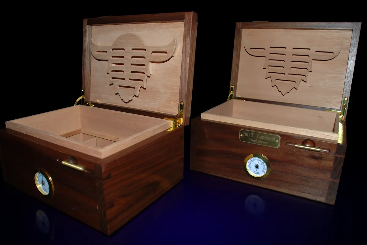Personalized walnut humidors with open lids with a personalized nameplate displayed on the front and a soft blue floor glow beneath