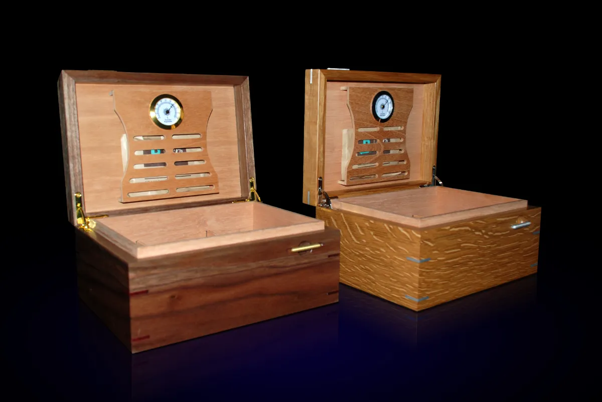 Open custom humidors in walnut and oak with matching Boveda holder designs. Walnut box displays brass hardware and Oak box displays aluminum hardware