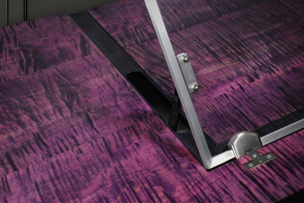 Close-up of a purple curly maple drafting desk showing the desktop grain and adjustable acrylic drafting table.