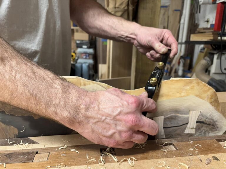 Woodworker using a spokeshave to shape a custom hardwood furniture piece
